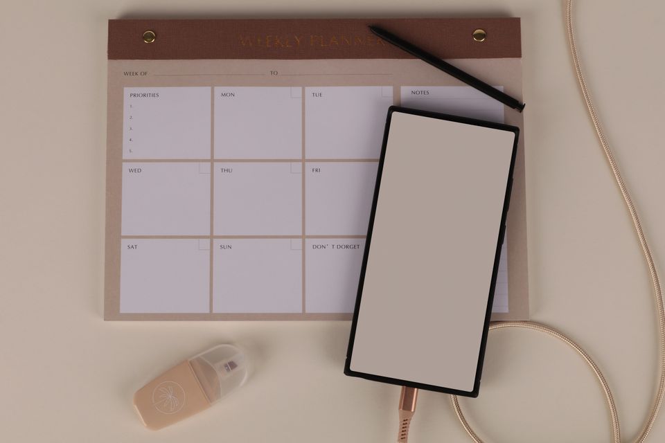 A weekly planner and phone arranged on a pale desk