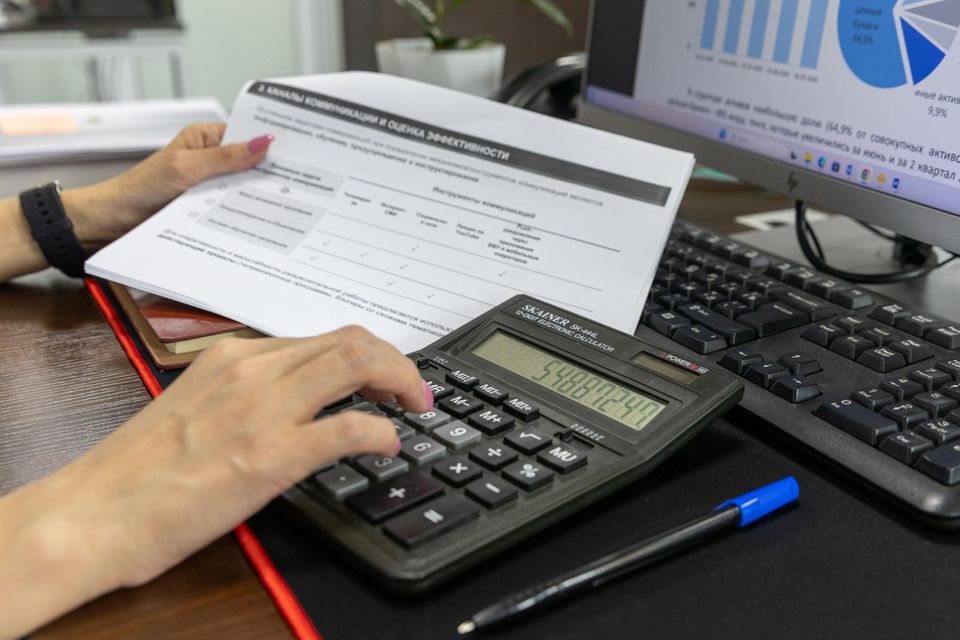 A calculator and financial report beside a chart on screen