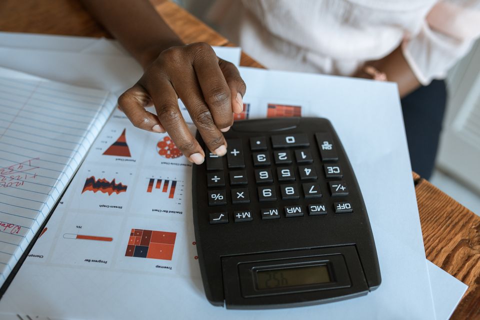 A hand using a calculator beside printed charts