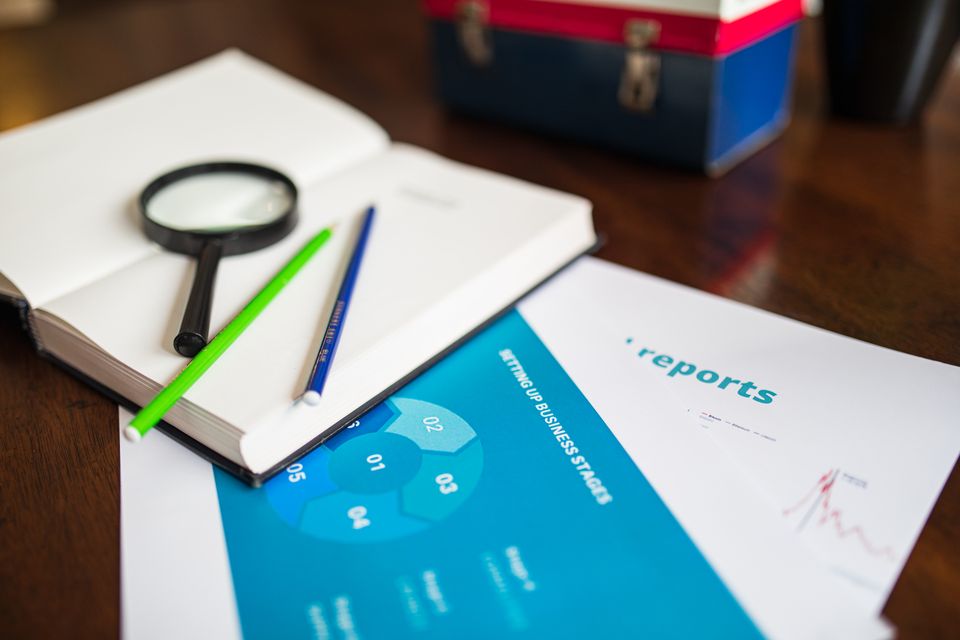 A magnifying glass beside a business report and pencils
